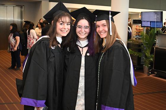 Photo of three young Chatham University female students in graduation robes and caps posing for a photo