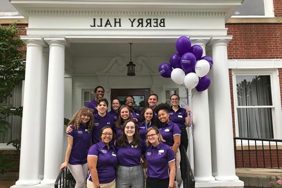 Photo of a group of Chatham University staff standing in front of Berry Hall wearing purple shirts and holding purple balloons. 