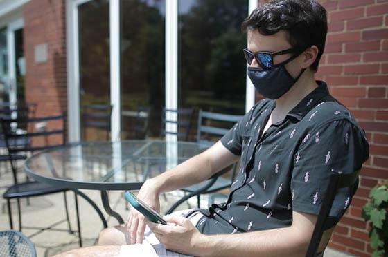 Photo of a Chatham University in a mask, outside, looking at his phone.