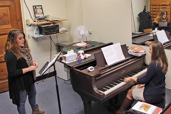 Photo of a Chatham University music student standing at a music stand singing next to a piano that is being played by an instructor.