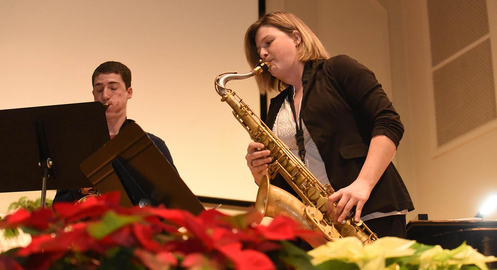 Photo of a woman playing a saxophone with poinsettas in the foreground